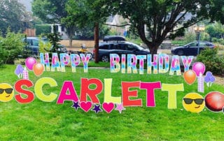 Happy Birthday Scarlett yard card with Tye-Dye letters and over-sized emoji's on a front lawn